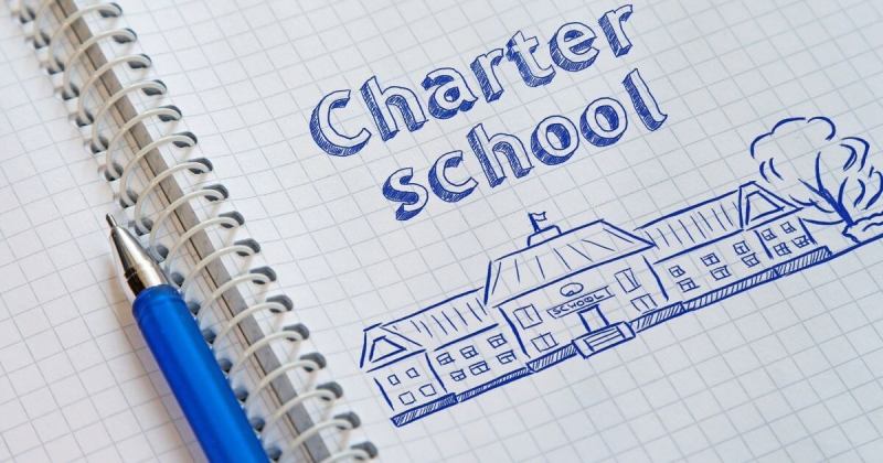 A stock image of a blank notebook with charter school written on it. Below the words is a drawing of a school building. All done in blue ink.