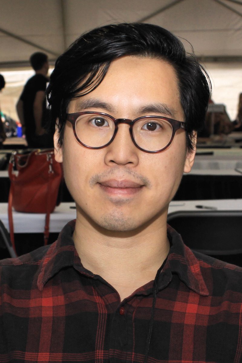 Close up photo of Tony Tulathimutte wearing a plaid shirt and glasses.