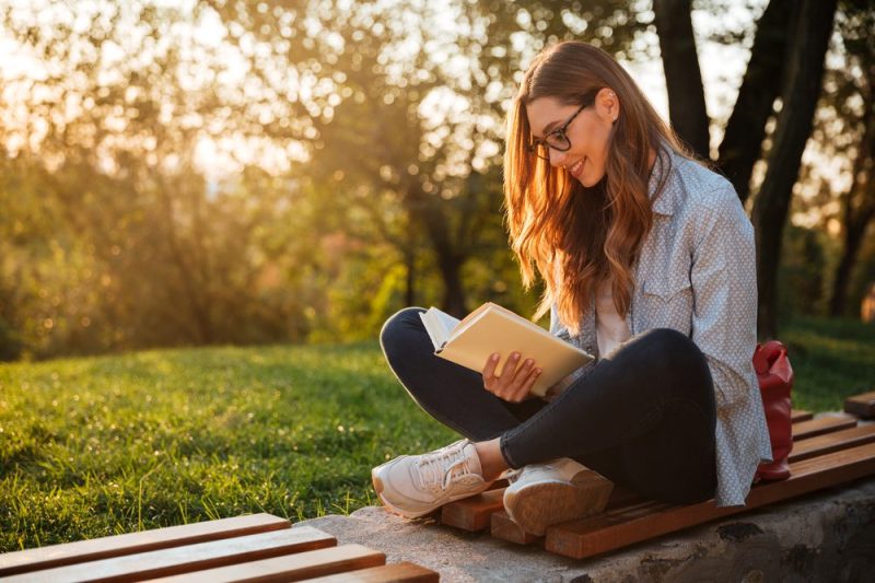 a woman sits outside and smiles while reading an iowa author